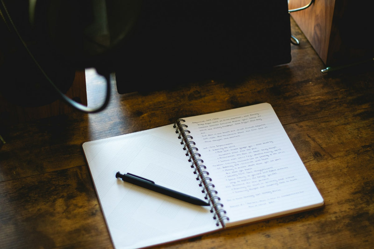 An open notebook and pen on a wooden desk in morning light